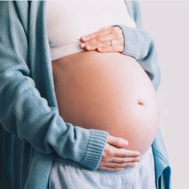 A pregnant woman in a blue cardigan with her hands on her bump